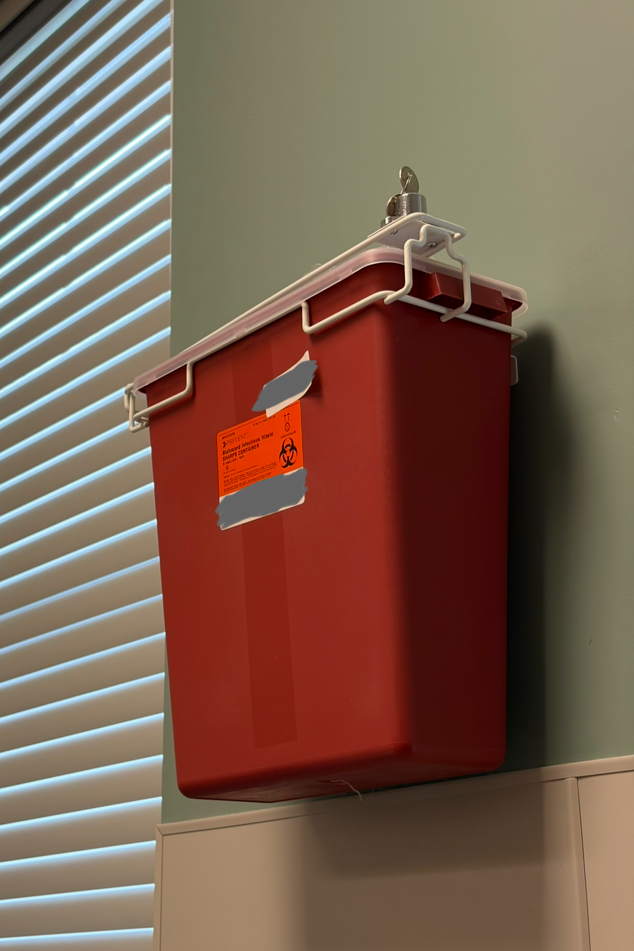 A sharps container mounted on a medical office wall with the key left in the lock